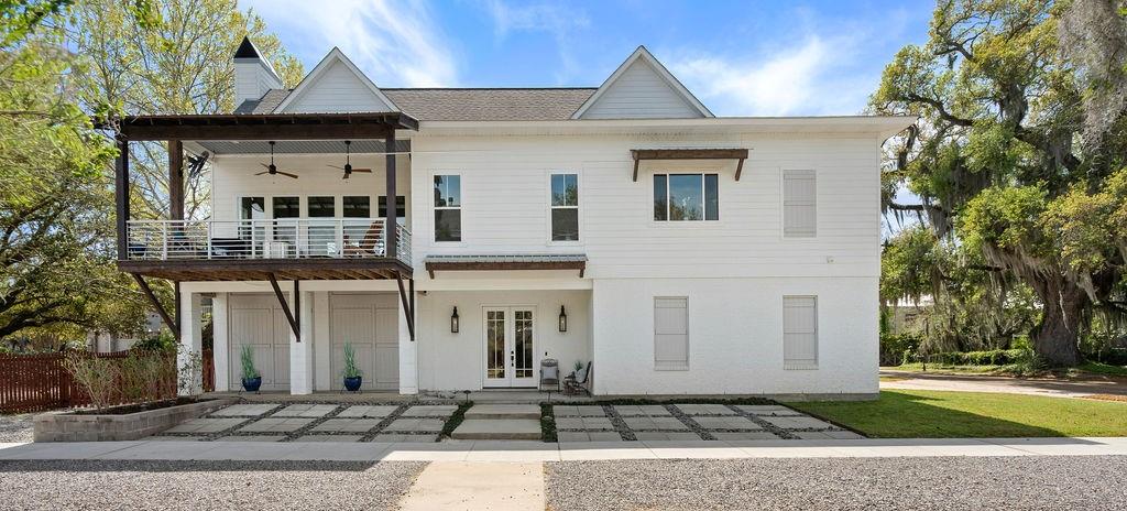 White two-story house with a covered balcony and geometric paved forecourt.