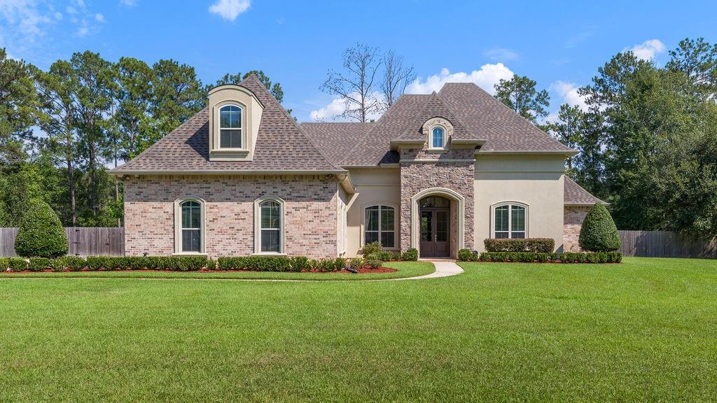 Two-story brick-and-stucco home with an arched entry, dormer window, and broad green lawn.