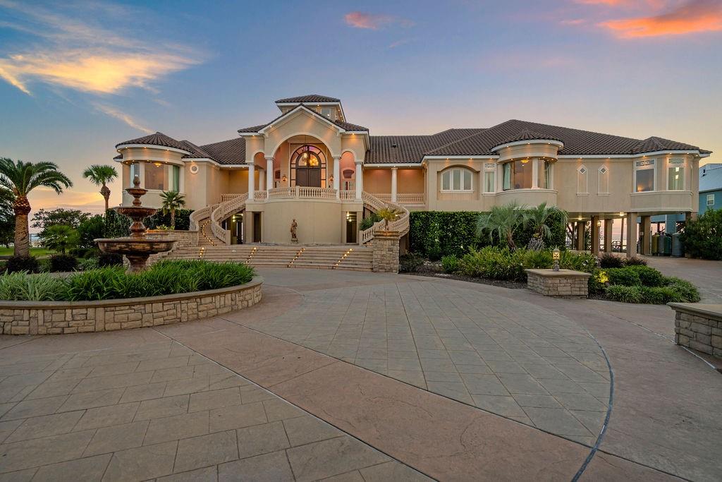 Large elevated home with a central arched entrance, broad staircases, and a fountain in the courtyard.