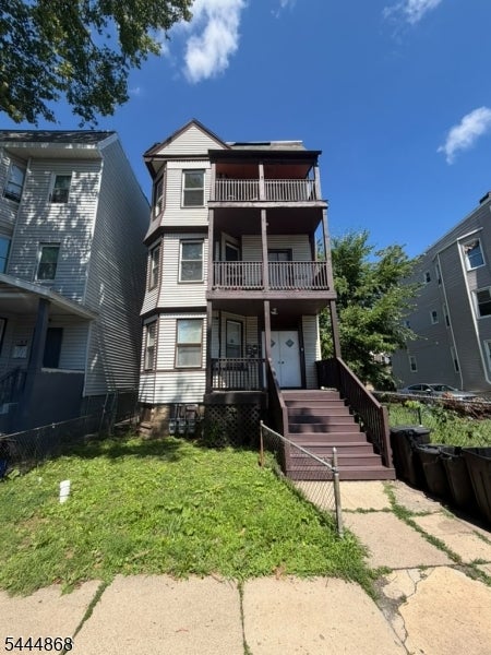 Three-story residential building with stacked porches and front steps beside a small grassy yard.