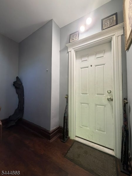 Entryway with a white paneled door, dark hardwood floors, and a sculptural figure beside the wall.