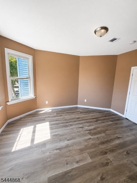 Vacant room with tan walls, gray wood-look flooring, and sunlight streaming through a window.