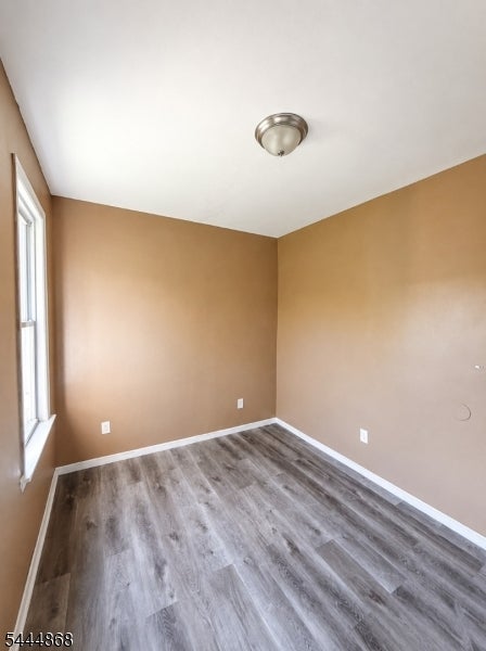 Vacant room with tan walls, gray wood-look flooring, and a window along one side.