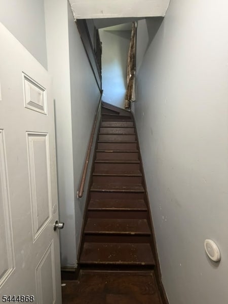 Narrow staircase with dark wood steps and a wooden handrail between light-colored walls.