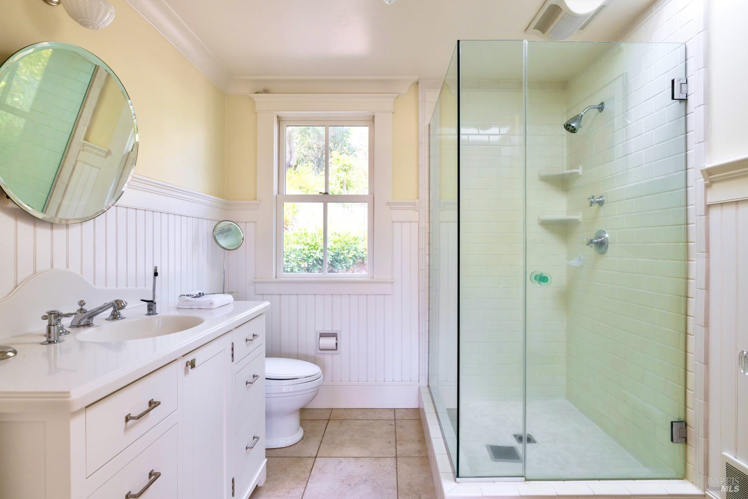 Bathroom with a white vanity and a spacious glass-enclosed shower beside a window.