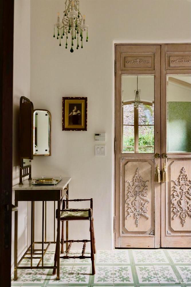 Entryway with carved double doors, an antique console and chair, and patterned tile flooring.