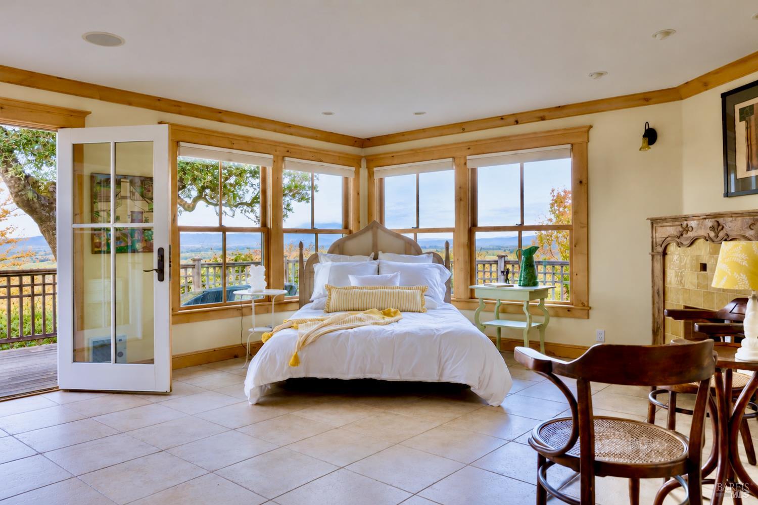 Bedroom with a white bed, wood-trimmed windows, and a balcony overlooking the countryside.