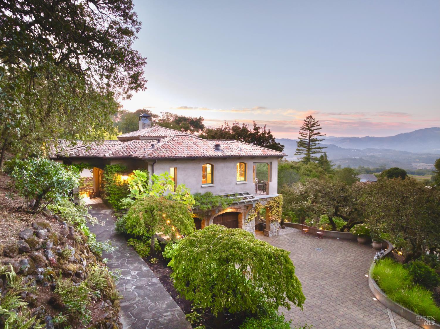 Stucco home with a tile roof, landscaped patio, and mountain valley views at sunset.