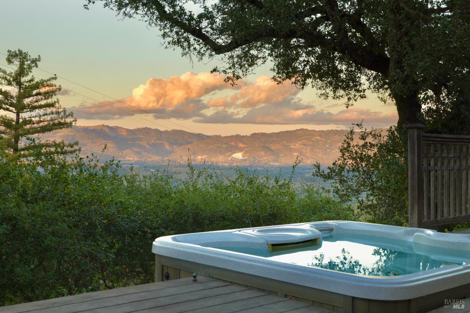 Outdoor hot tub overlooking wooded hills and distant mountains at sunset.