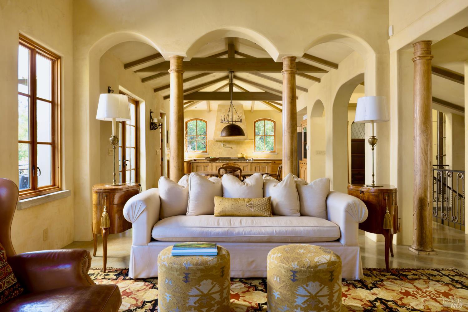 Living room with a white sofa beneath exposed beams, framed by arches and wood columns.