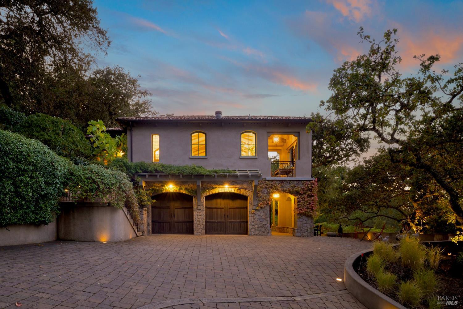 Home exterior with stone-arched garage doors and illuminated windows at dusk.