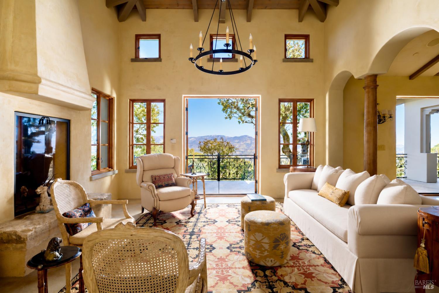 Living room with a stone fireplace, vaulted beam ceiling, and mountain views through the open doorway.