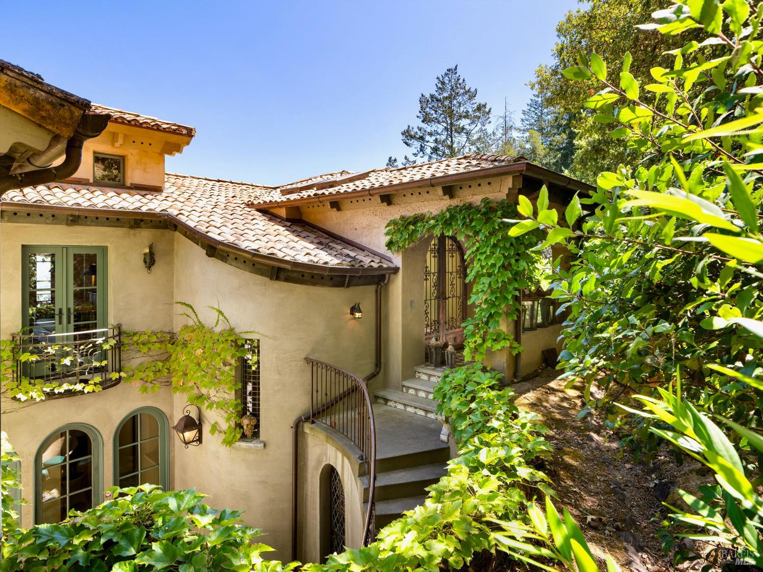 Stucco home with a terracotta tile roof, arched entrance, curved steps, and leafy landscaping.