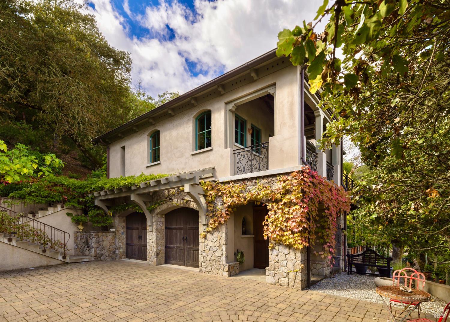Two-story stone-and-stucco home with a vine-covered facade, balcony, and paved courtyard.