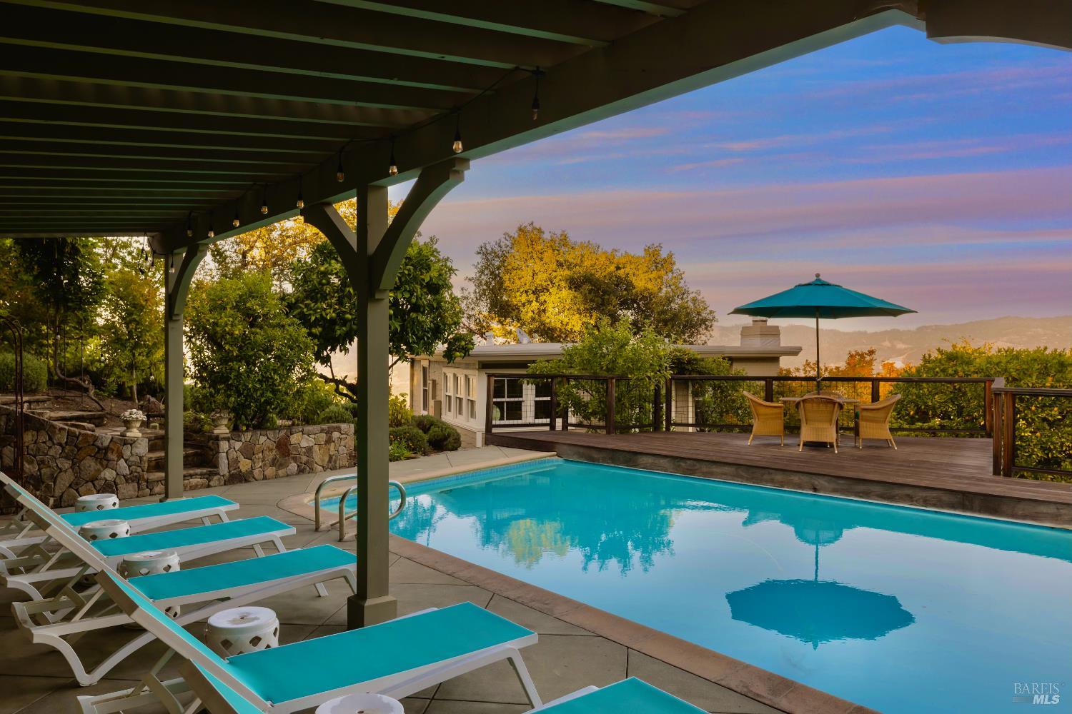 Outdoor pool beneath a pergola, with turquoise loungers and distant hills in the sunset light.
