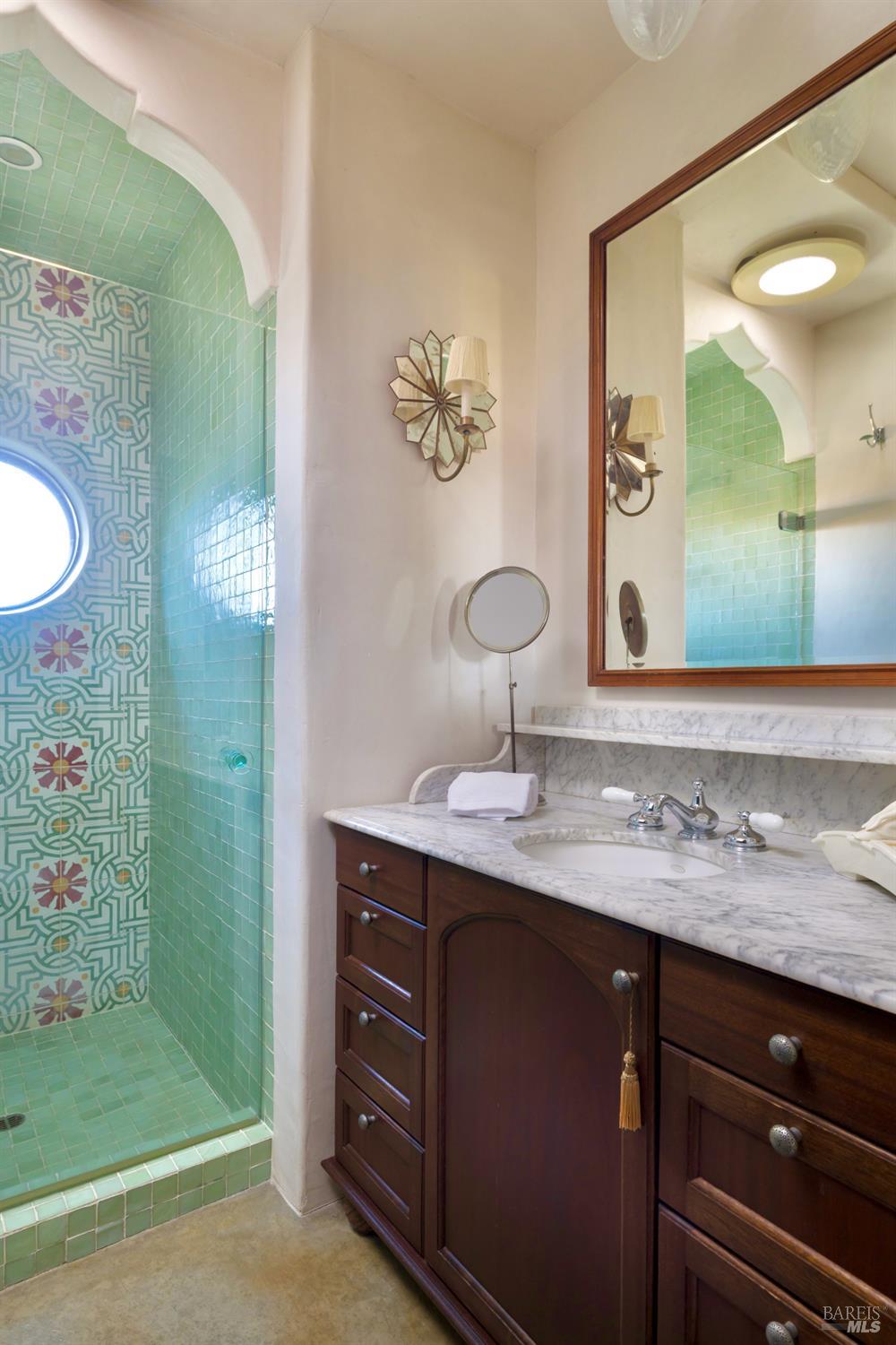 Bathroom with a turquoise patterned-tile shower and dark wood vanity topped with marble.