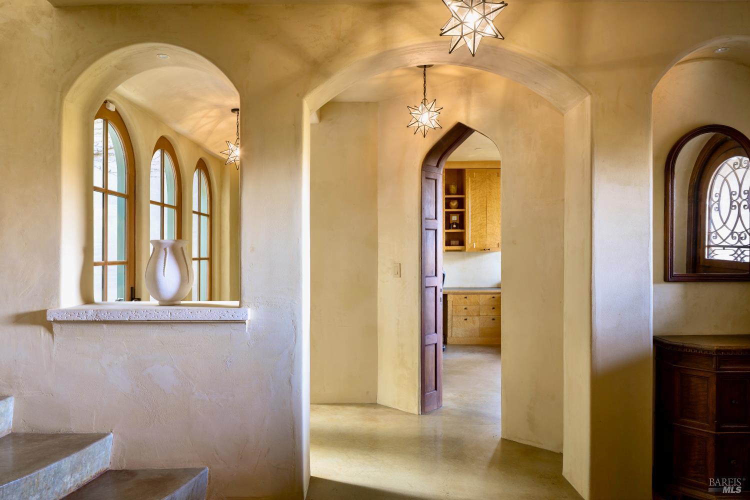 Arched entry hall with tall windows, star-shaped pendant lights, and a view into the kitchen.