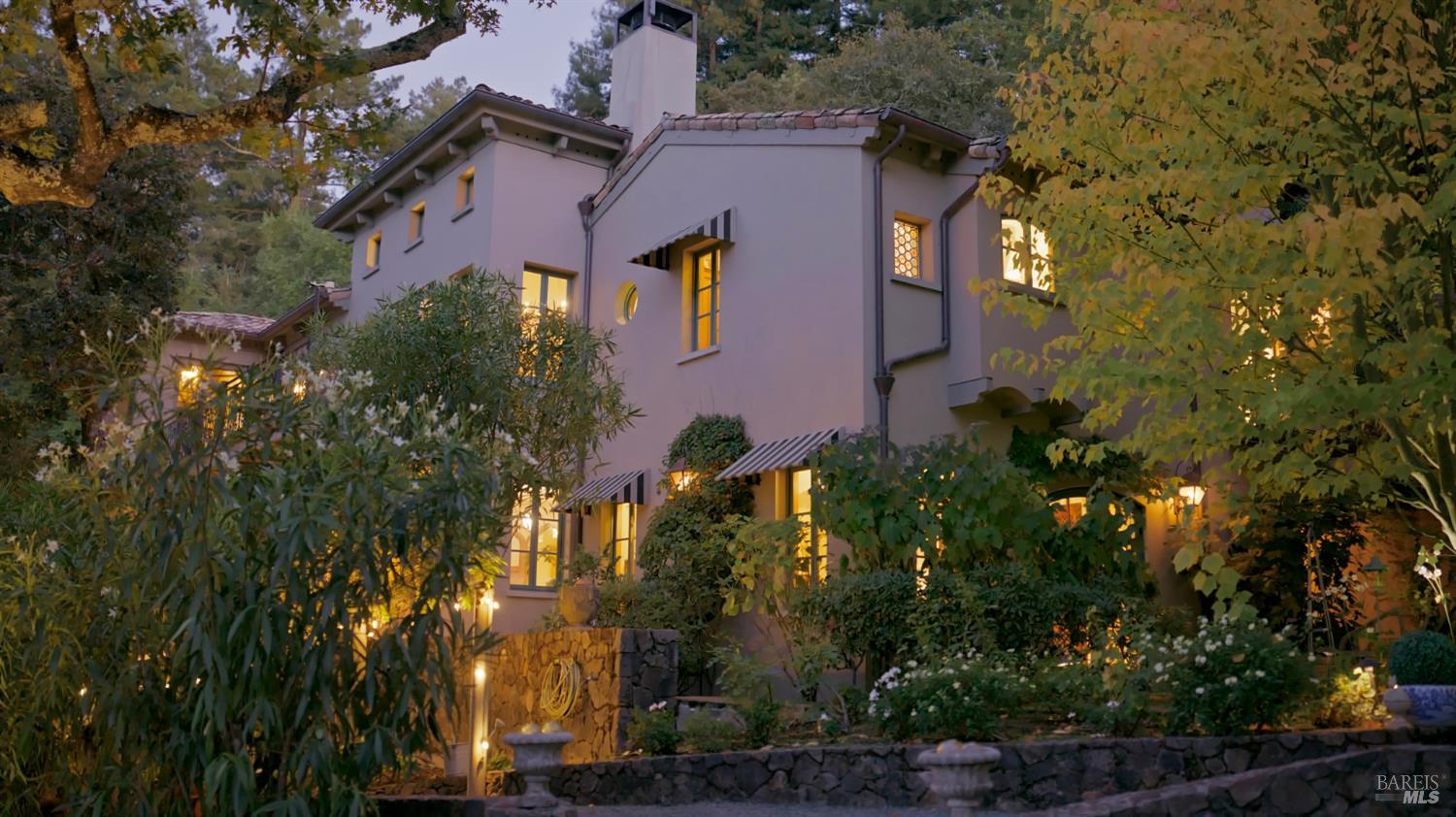 Stucco home at dusk, framed by autumn foliage and landscaped gardens with stone retaining walls.