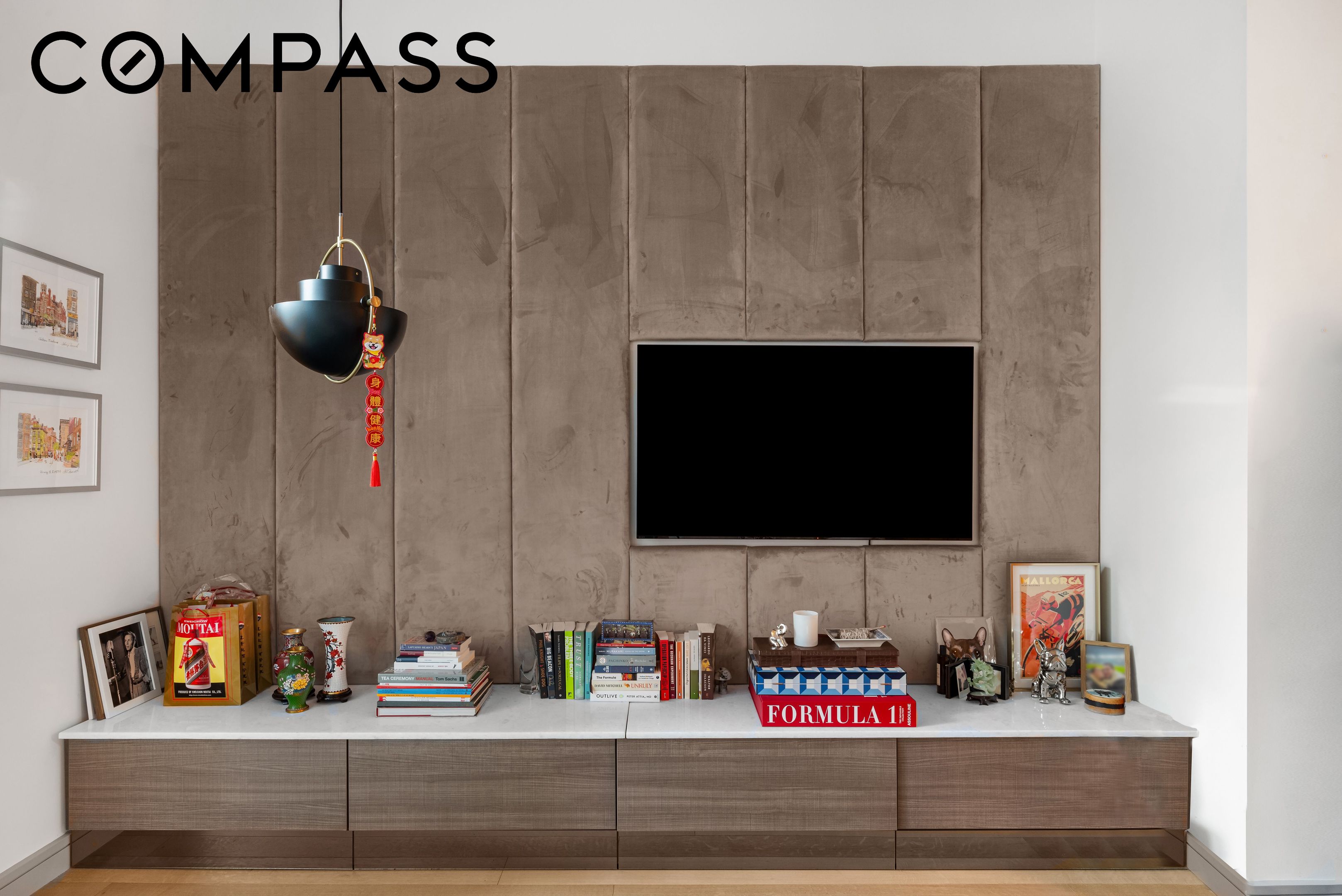 Living room media wall with a television, taupe textured panels, and a long cabinet lined with books and art.