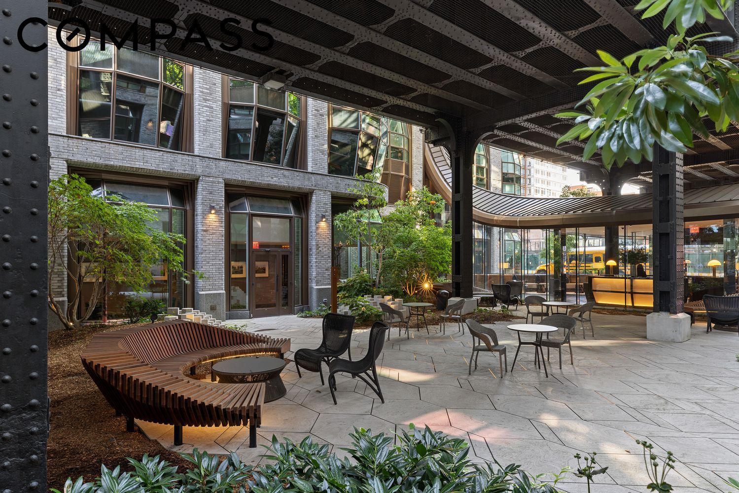 Residential courtyard with a curved wooden bench, outdoor seating, greenery, and a glass-fronted lobby.