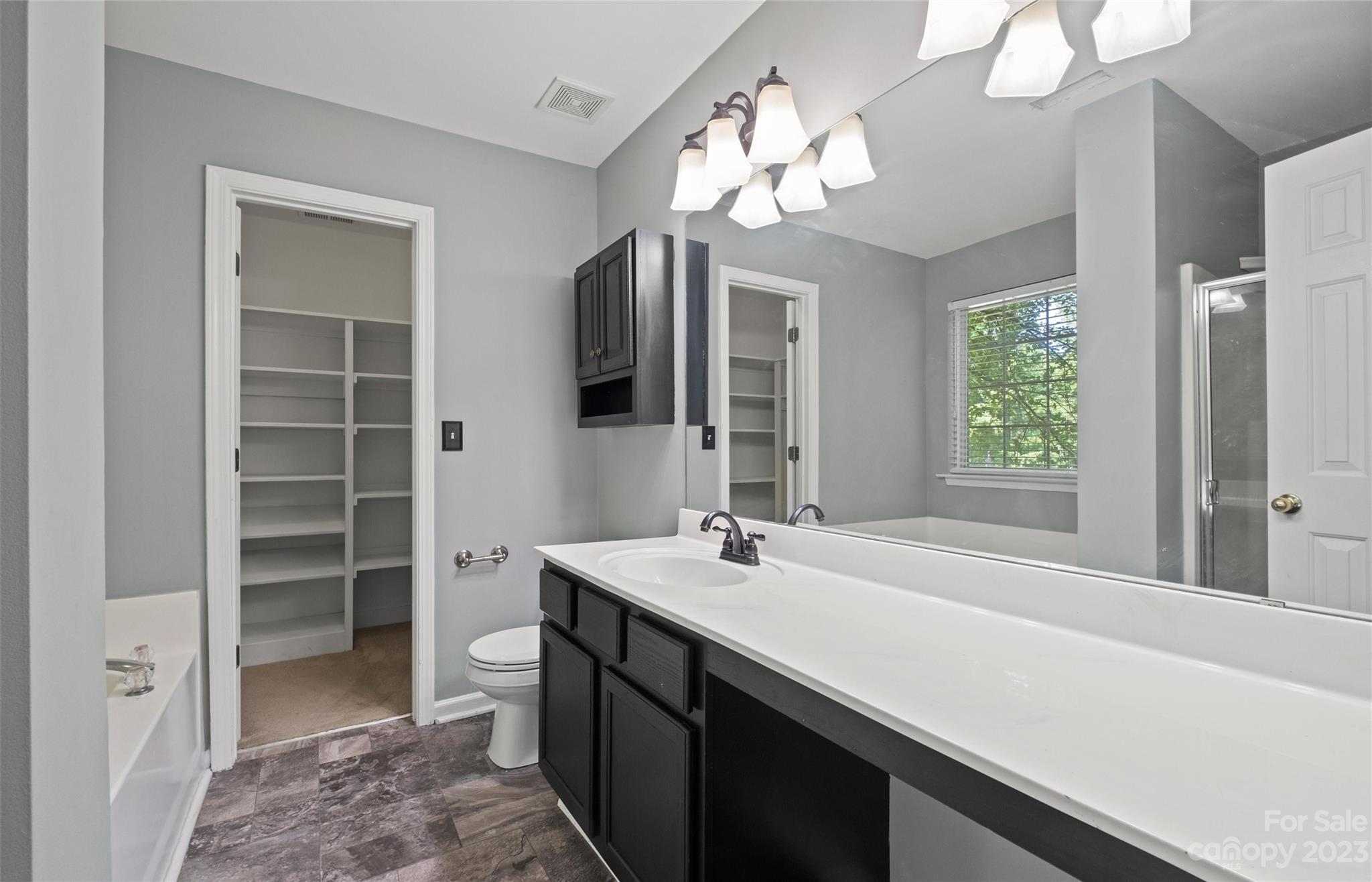 Bathroom with a long white vanity, dark cabinets, large mirror, and open shelving closet.