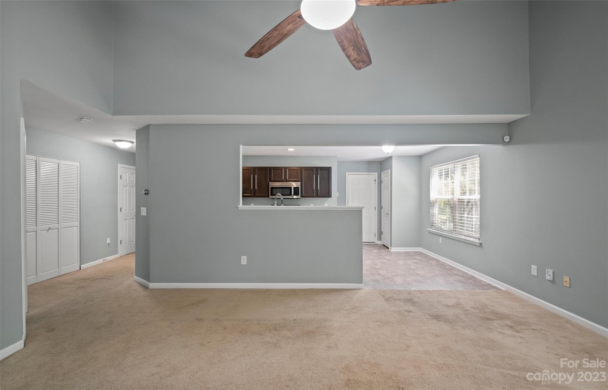 Empty living room with vaulted ceiling, beige carpet, and a pass-through to the kitchen.