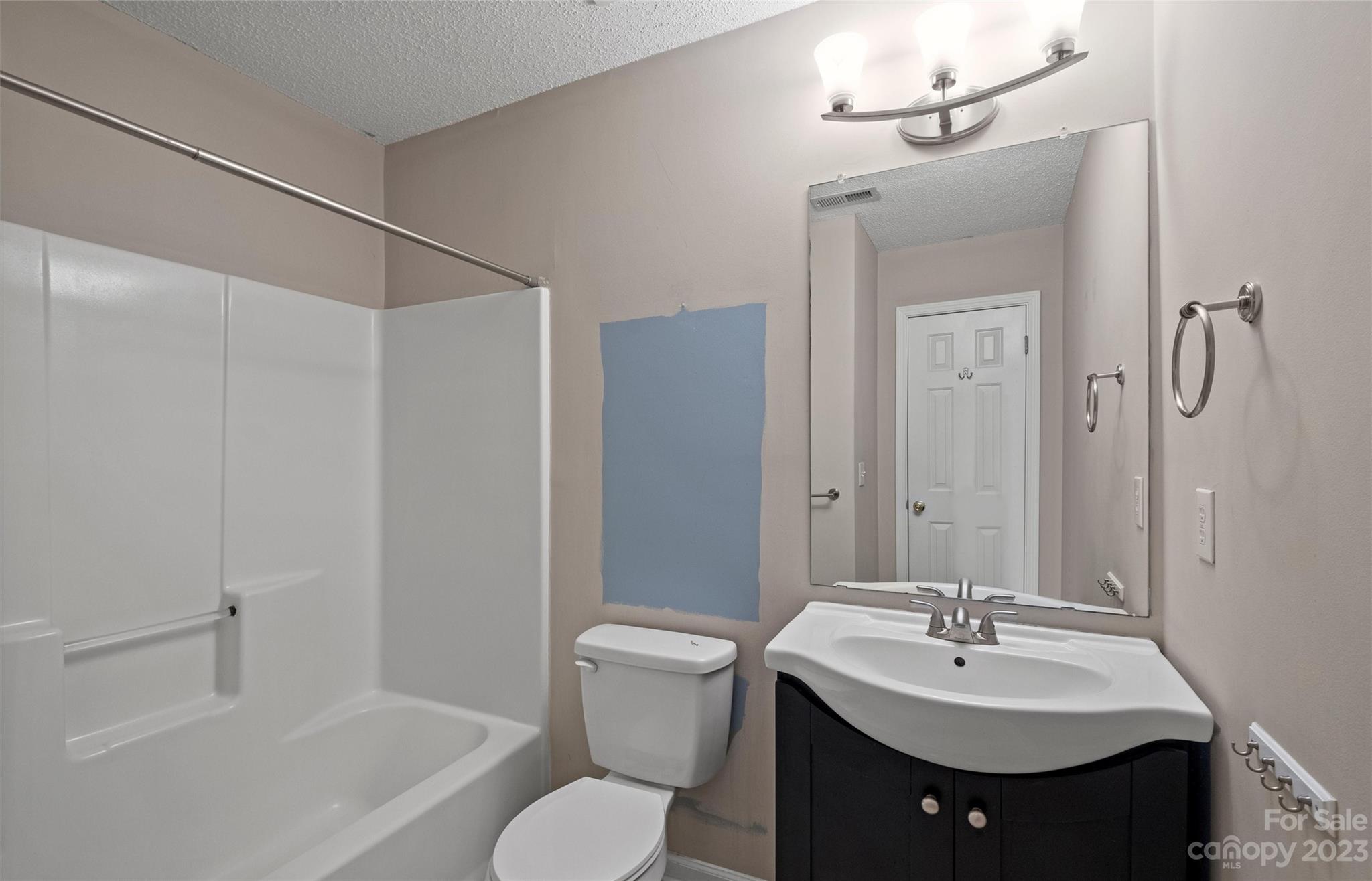 Bathroom with a white tub and shower beside a dark vanity, large mirror, and blue paint sample.