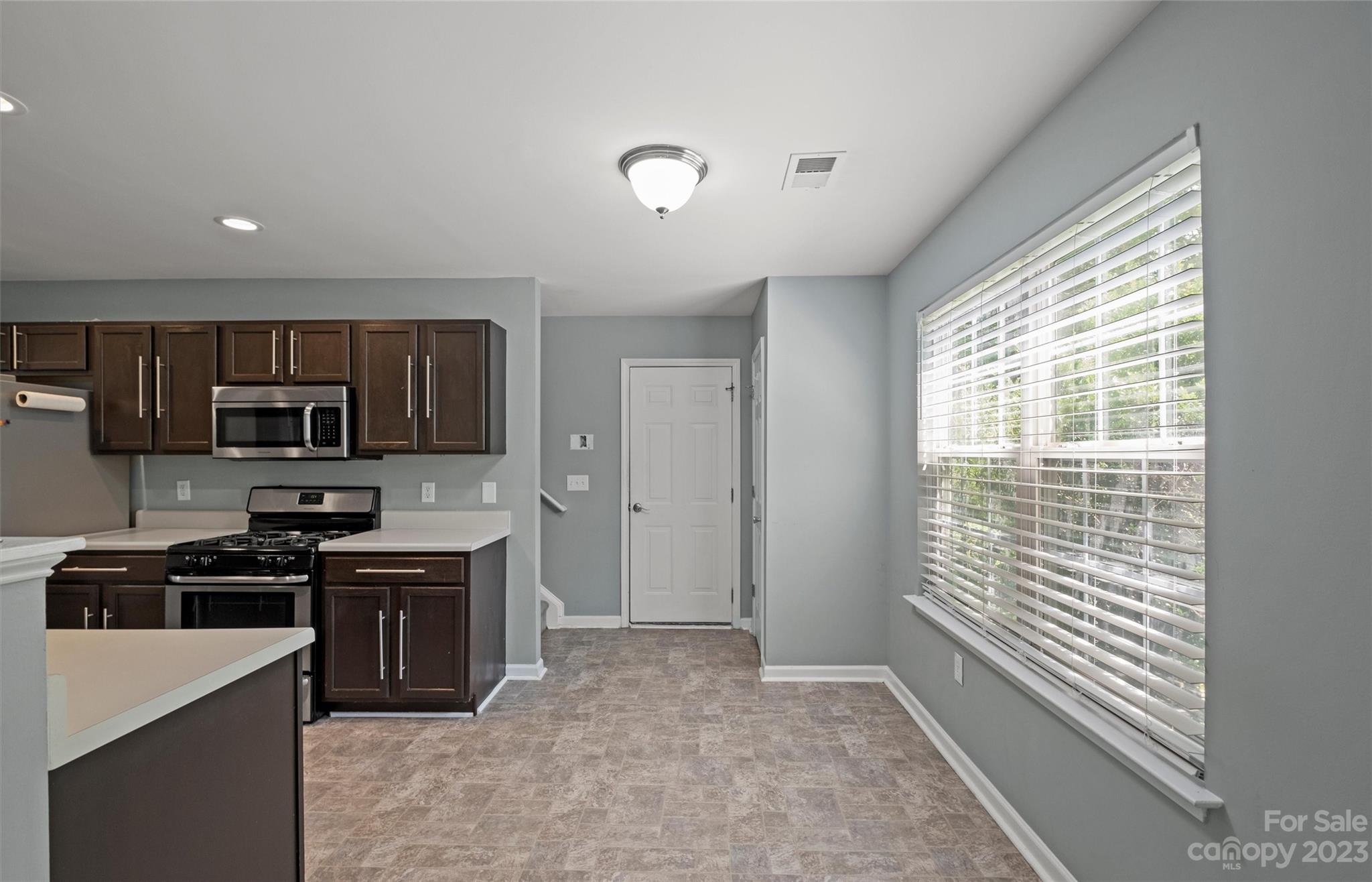 Kitchen with dark cabinets, stainless steel appliances, patterned tile flooring, and a large window with blinds.