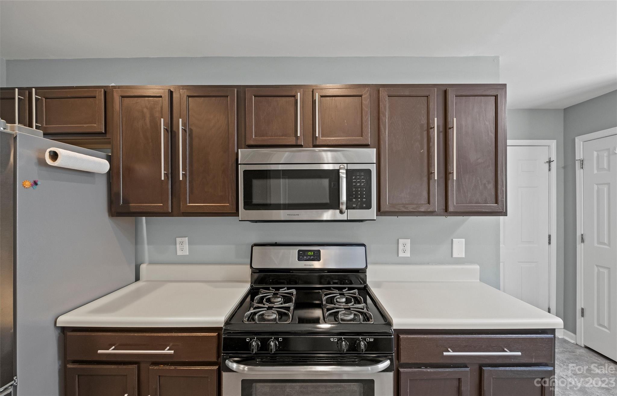 Kitchen with dark wood cabinets, white countertops, and a black gas range beneath a stainless steel microwave.