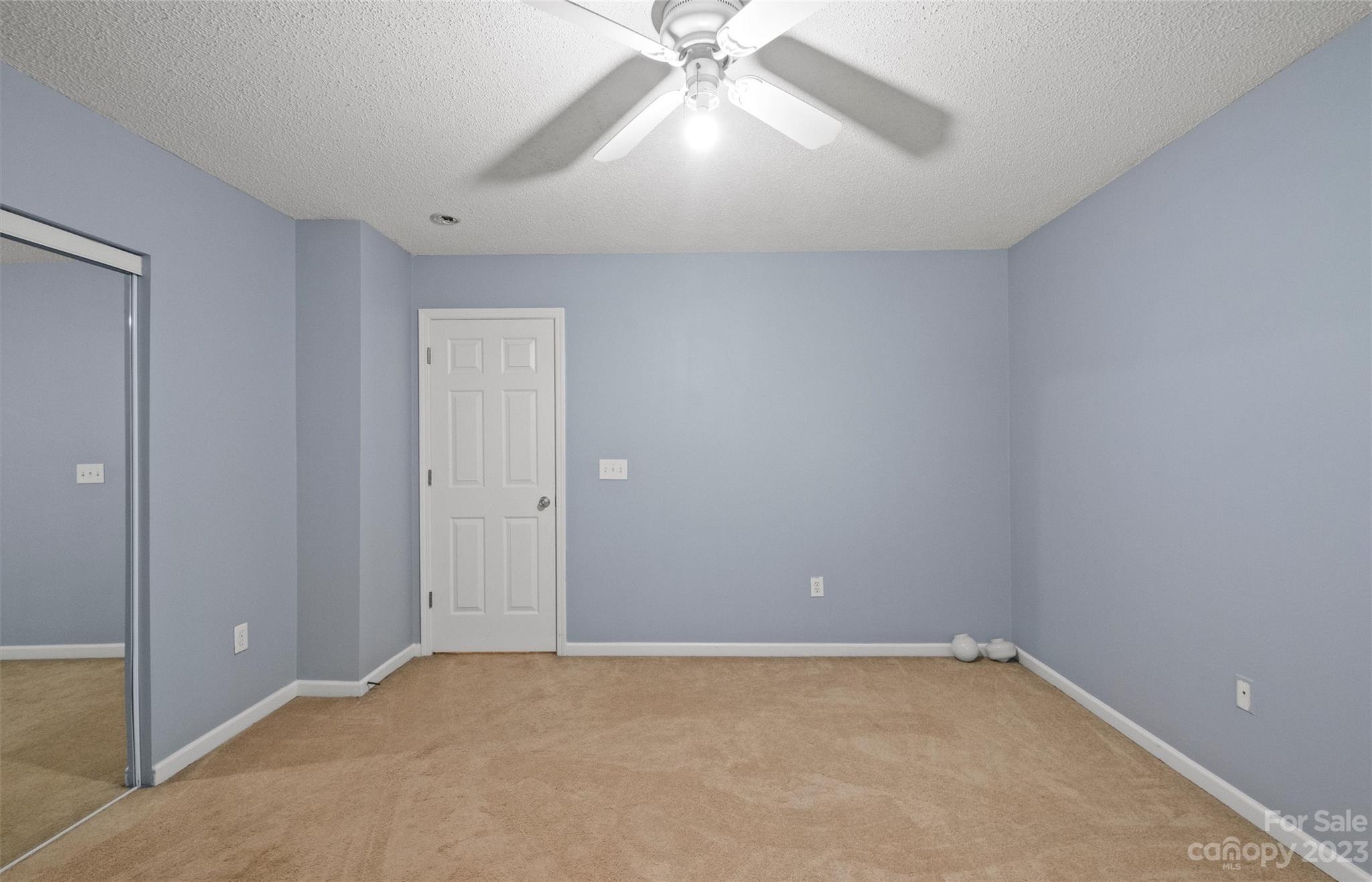 Vacant bedroom with beige carpet, pale blue walls, ceiling fan, and mirrored closet doors.