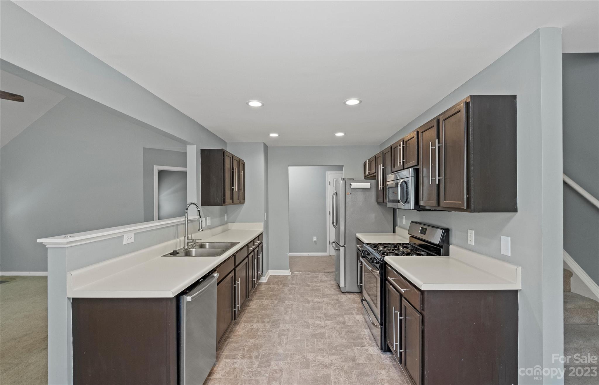 Kitchen with dark cabinets, light countertops, stainless steel appliances, and a double-basin sink.