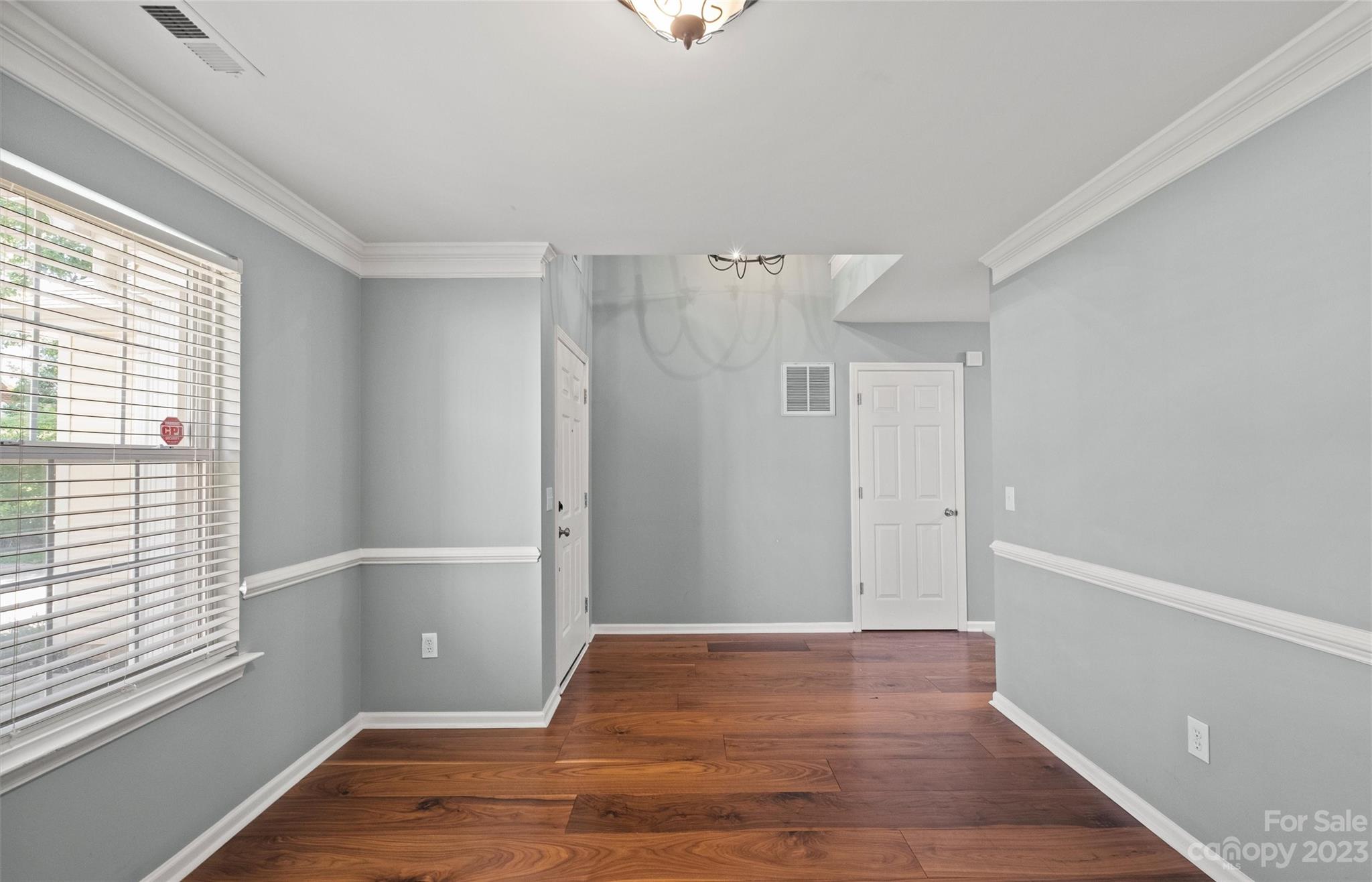 Empty gray interior room with hardwood floors, white trim, and a large window with blinds.