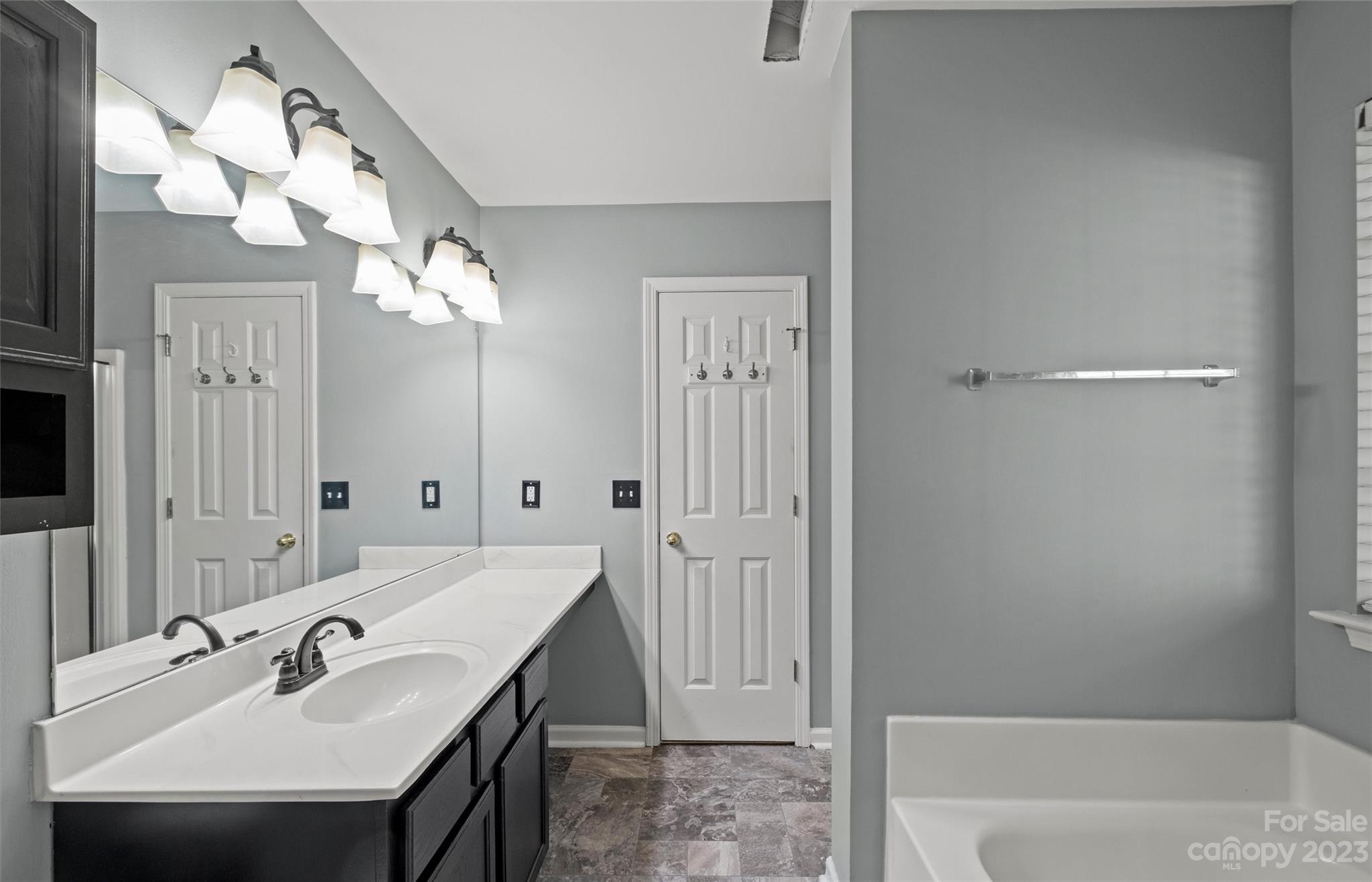 Bathroom with a white double vanity, large mirror, gray walls, and adjacent bathtub.