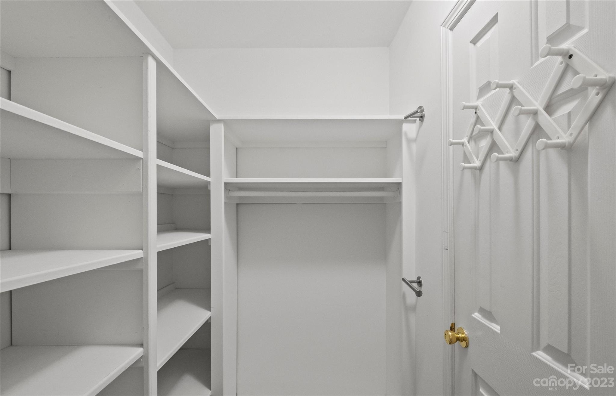 Walk-in closet with built-in white shelves, a hanging rod, and folding wall hooks.