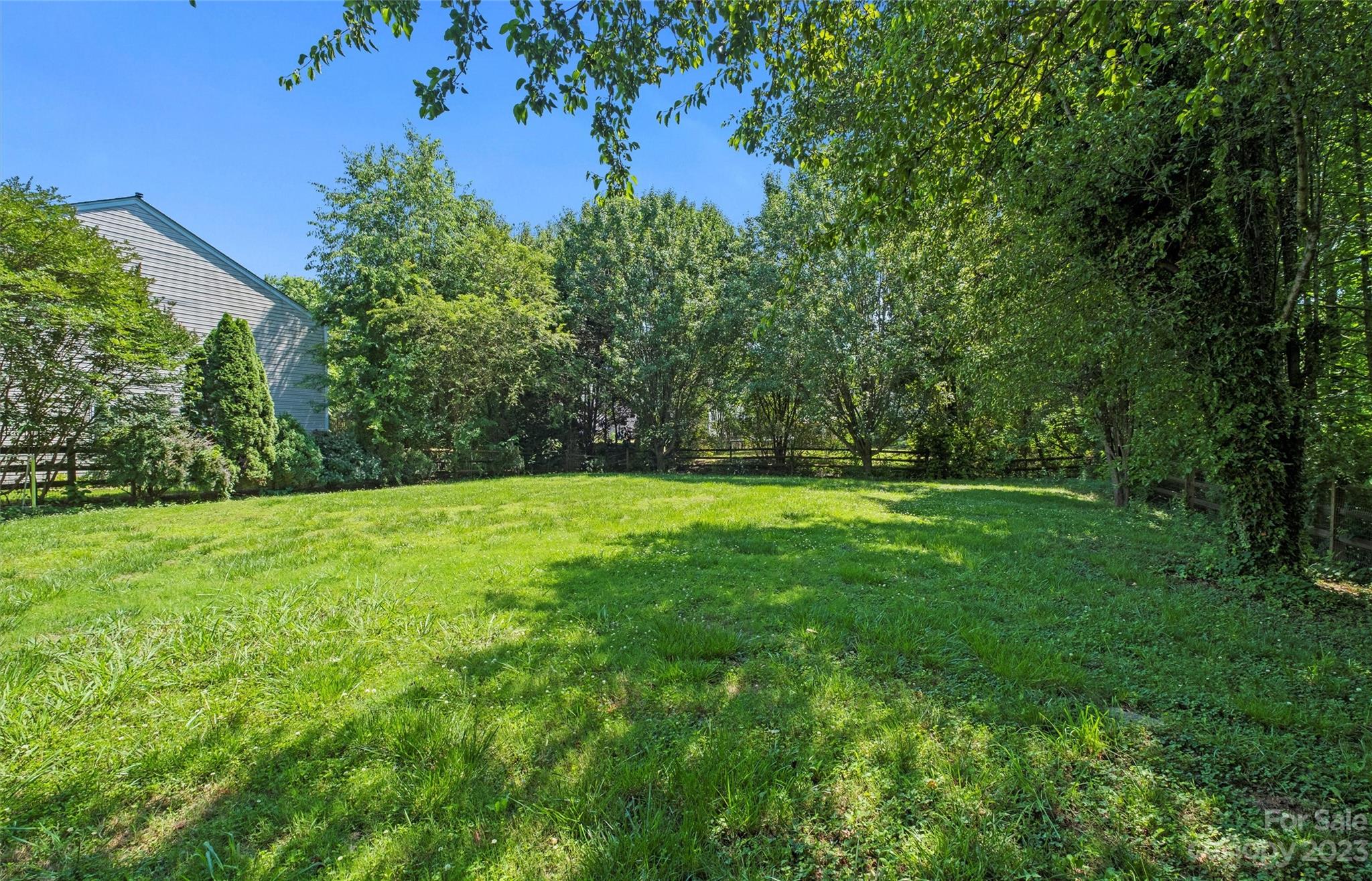 Backyard lawn bordered by mature trees and shrubs, with a wooden fence.