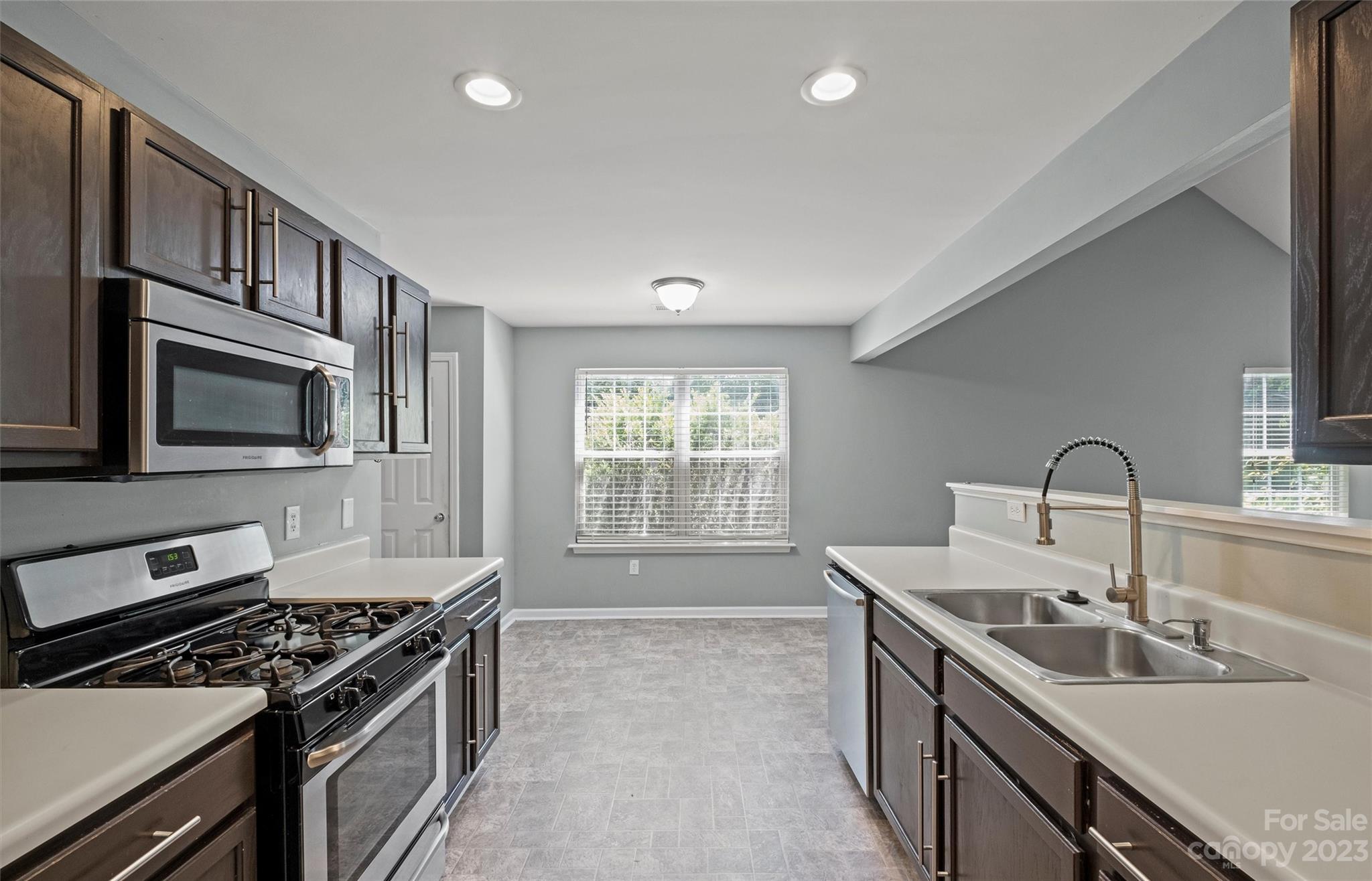 Kitchen with dark wood cabinets, a gas range, white counters, and a double-basin sink.