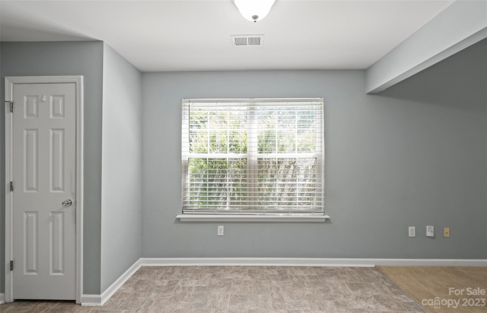Vacant room with gray walls, tiled flooring, and a large window with white blinds.