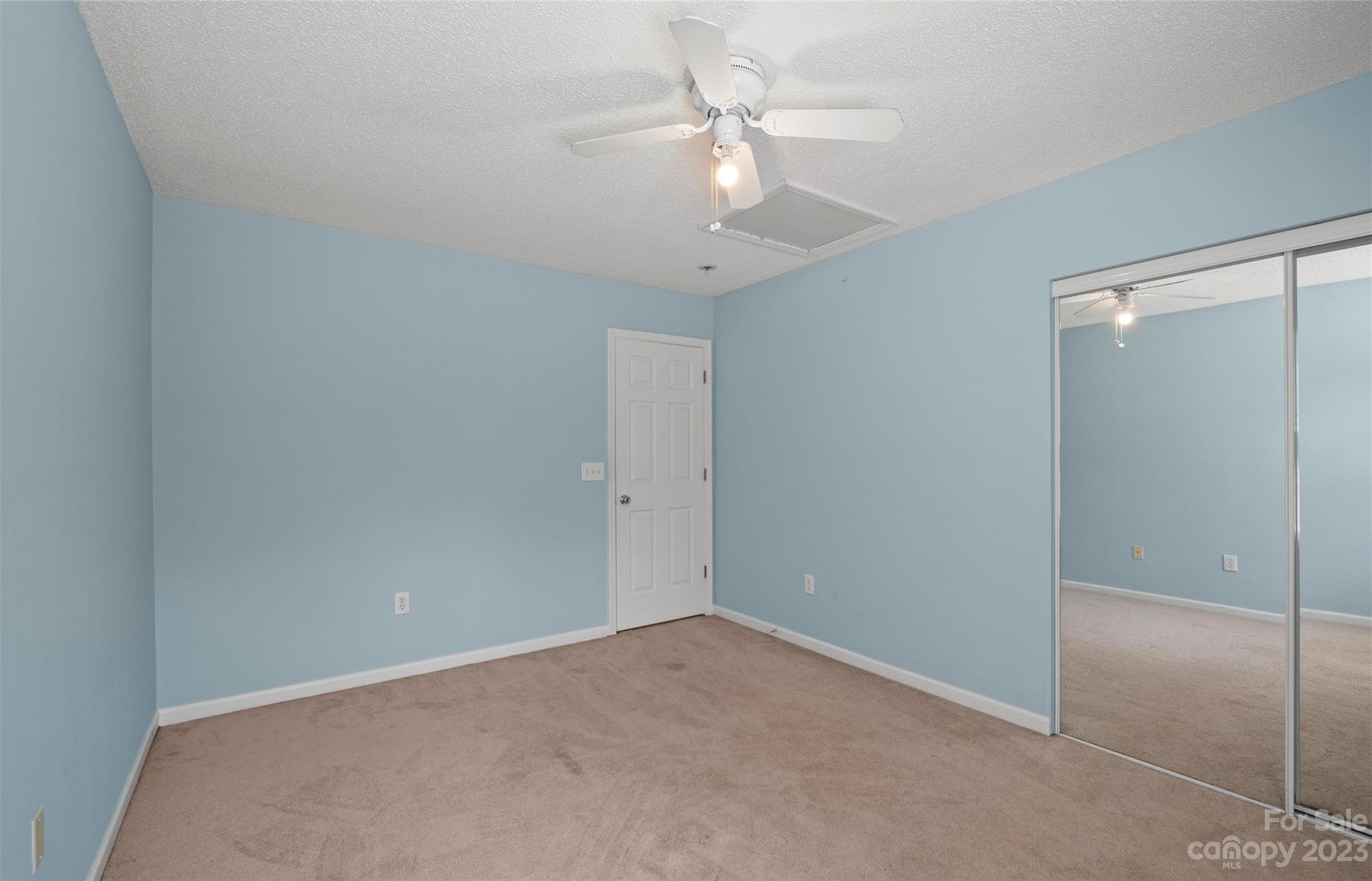 Empty bedroom with blue walls, beige carpet, and mirrored sliding closet doors.