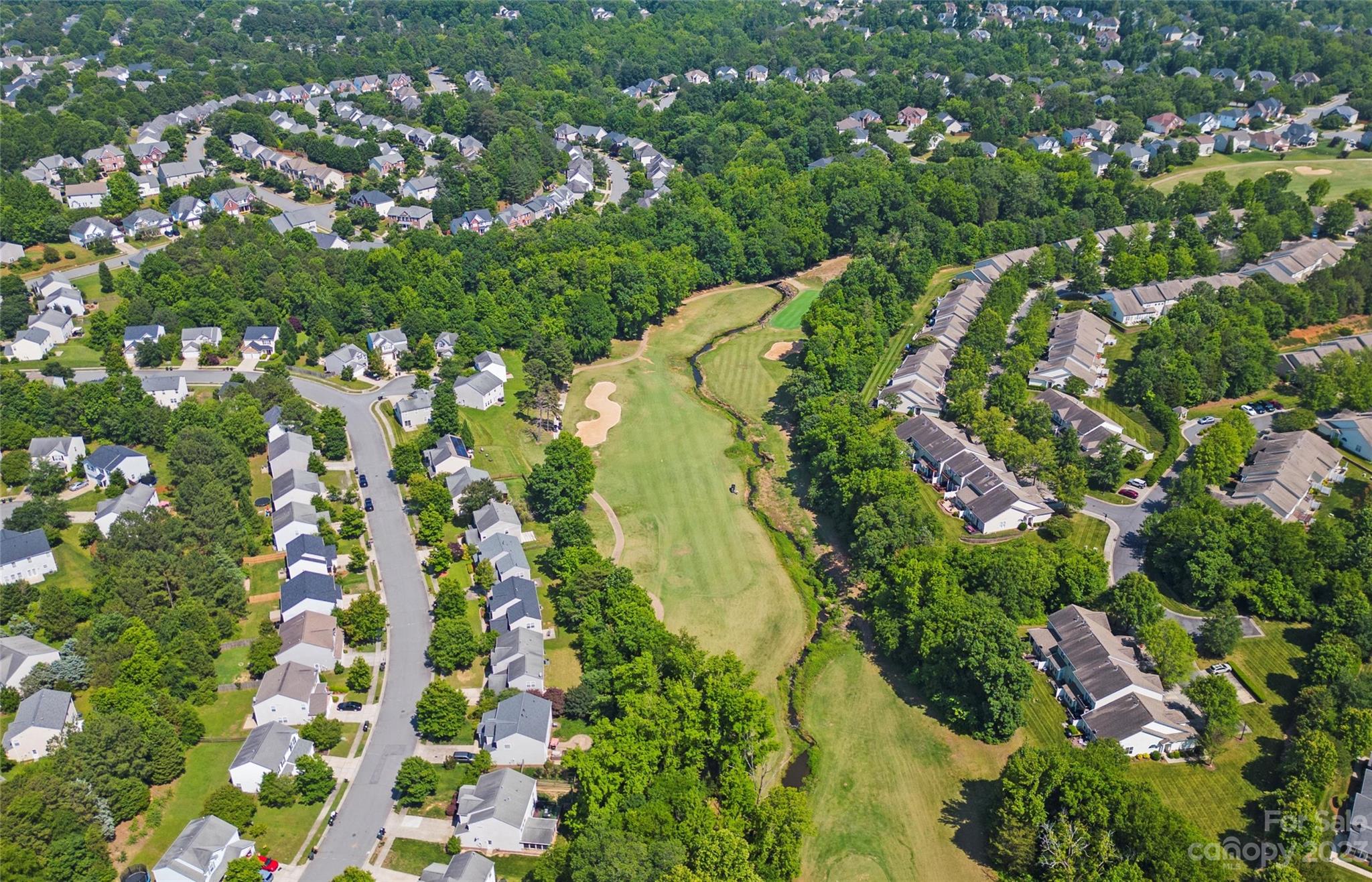 Aerial view of a golf course winding through a tree-lined residential neighborhood.