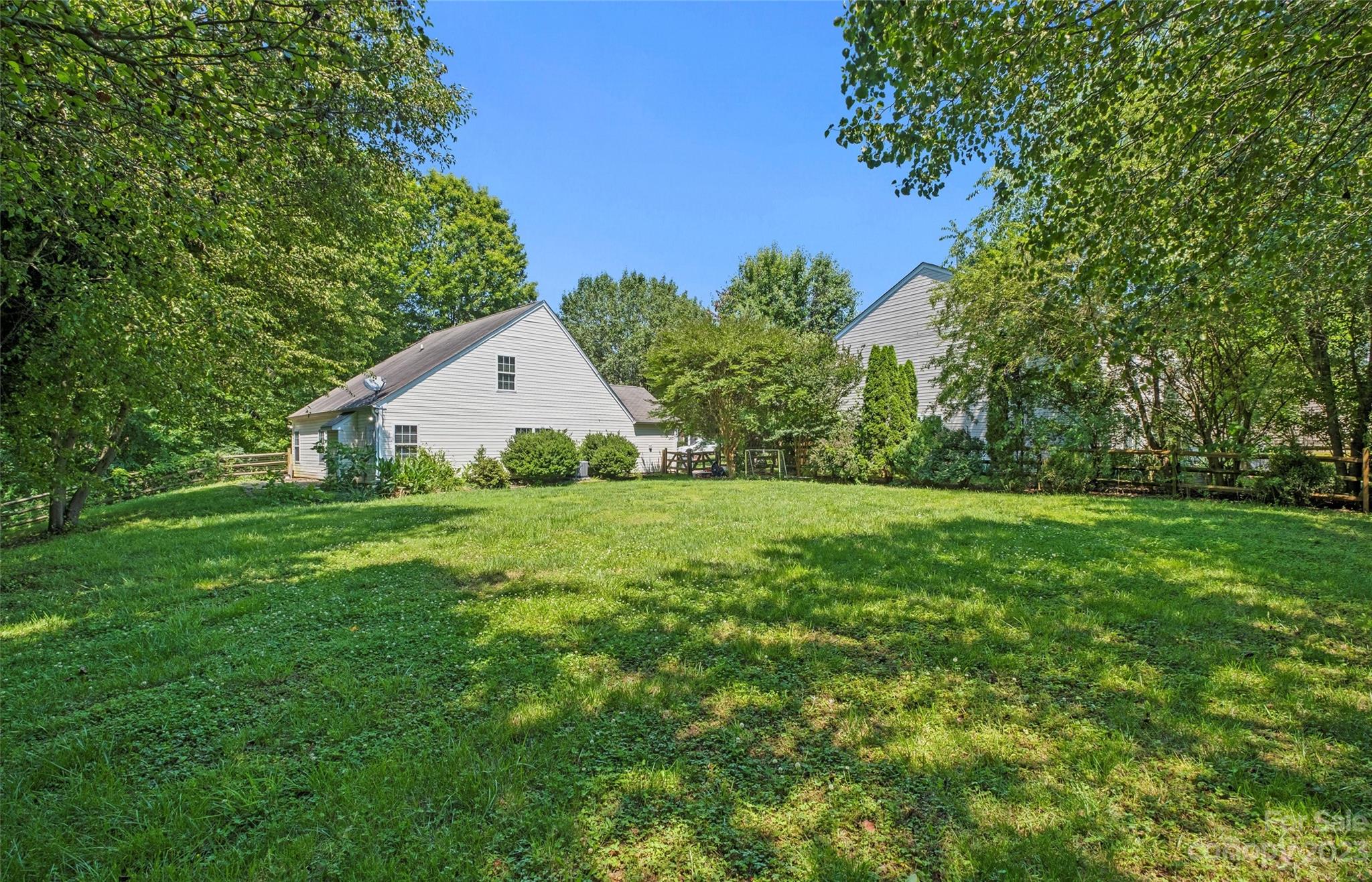 Light-sided house behind a broad lawn, framed by mature trees and shrubs.