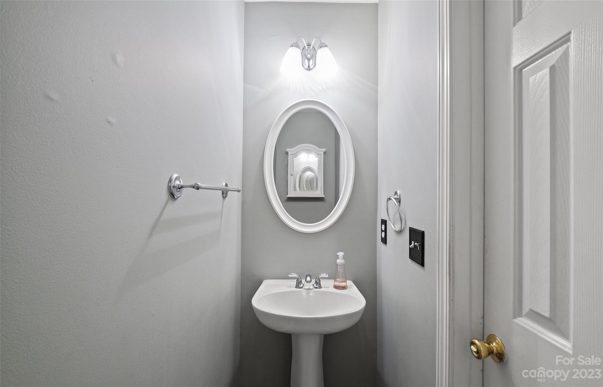 Bathroom with a pedestal sink, oval mirror, and chrome fixtures.