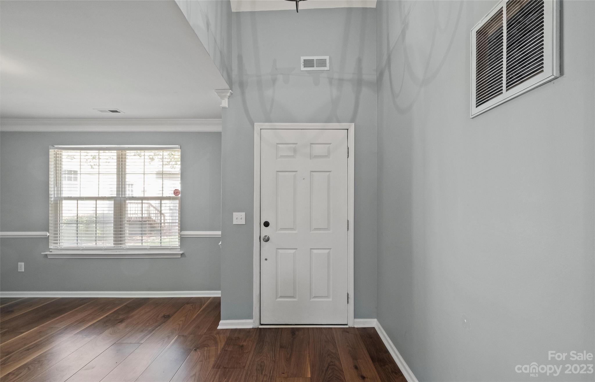 Empty entryway with a white paneled front door, gray walls, and dark wood floors.