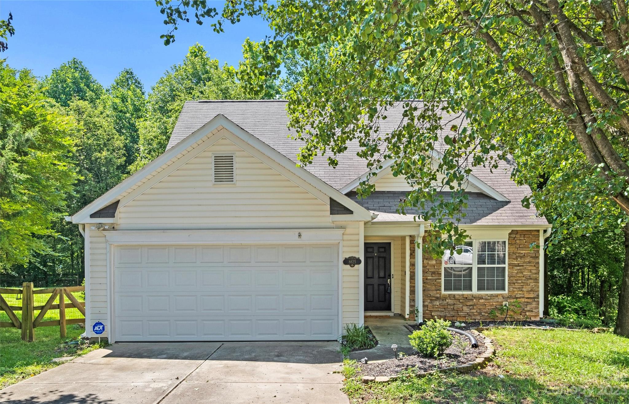 House with a stone facade, double garage, and leafy trees framing the front yard.