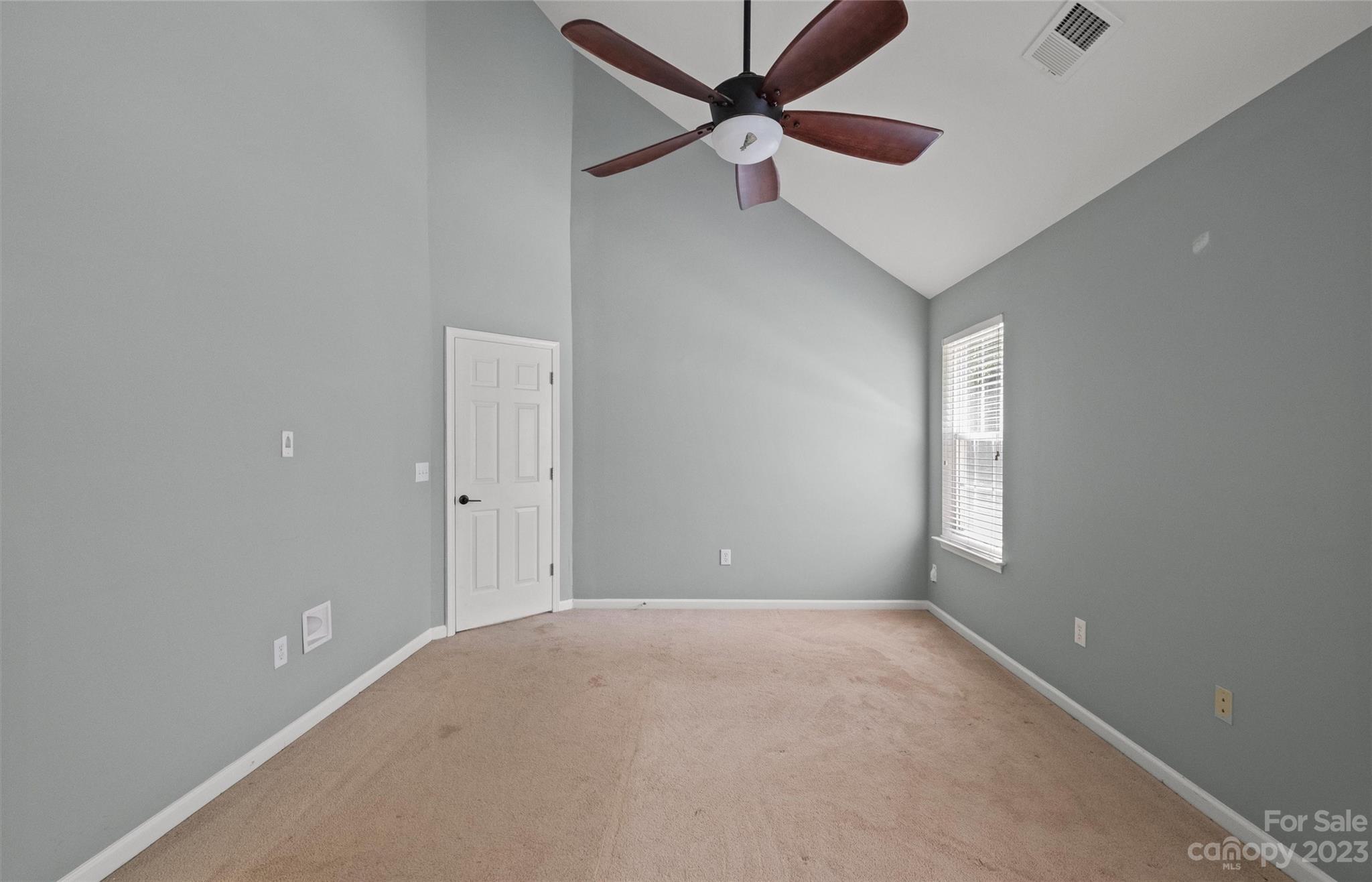 Empty carpeted room with gray walls, a vaulted ceiling, and a dark wood ceiling fan.