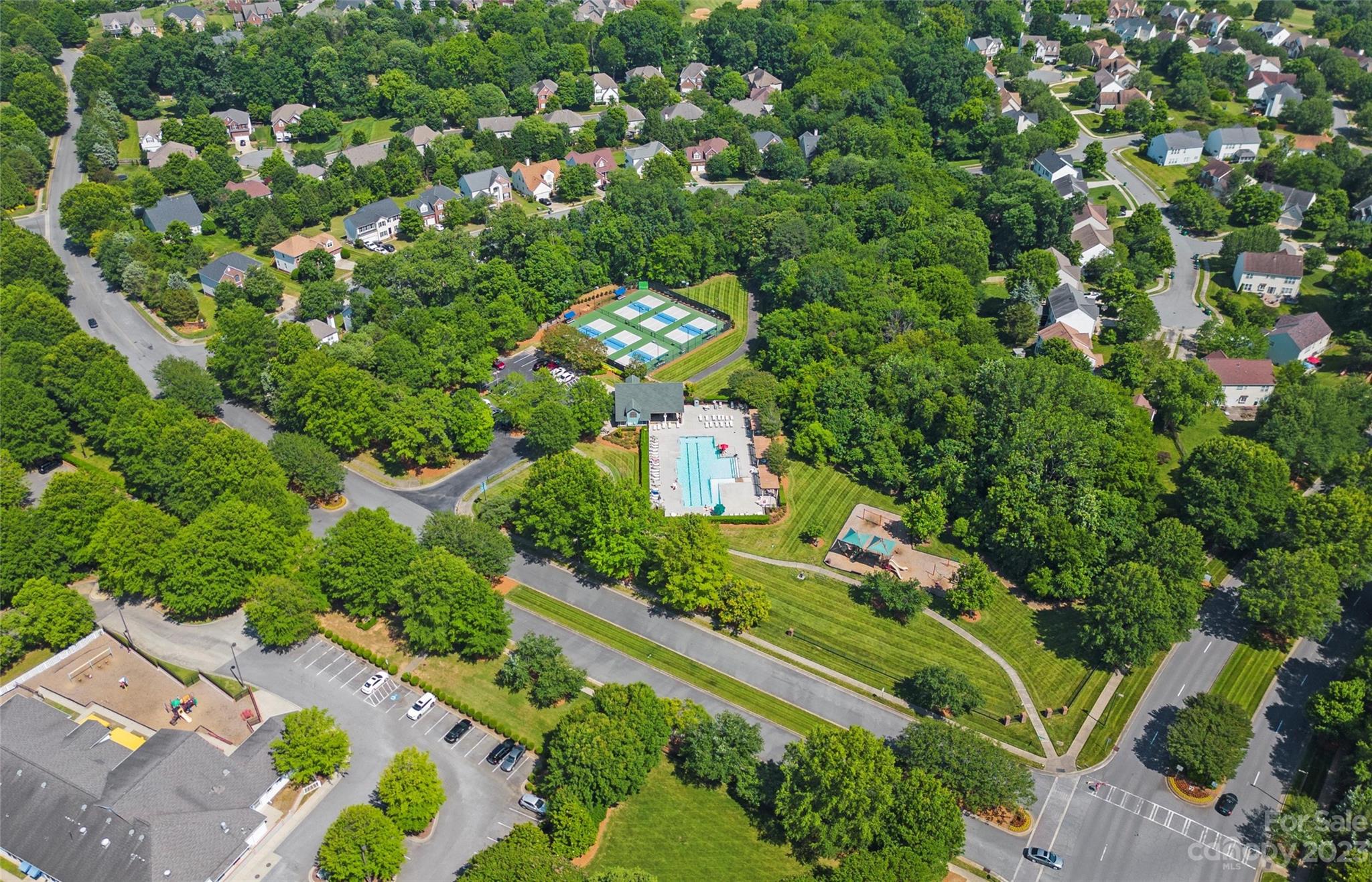 Aerial view of a wooded neighborhood with a swimming pool and tennis courts.