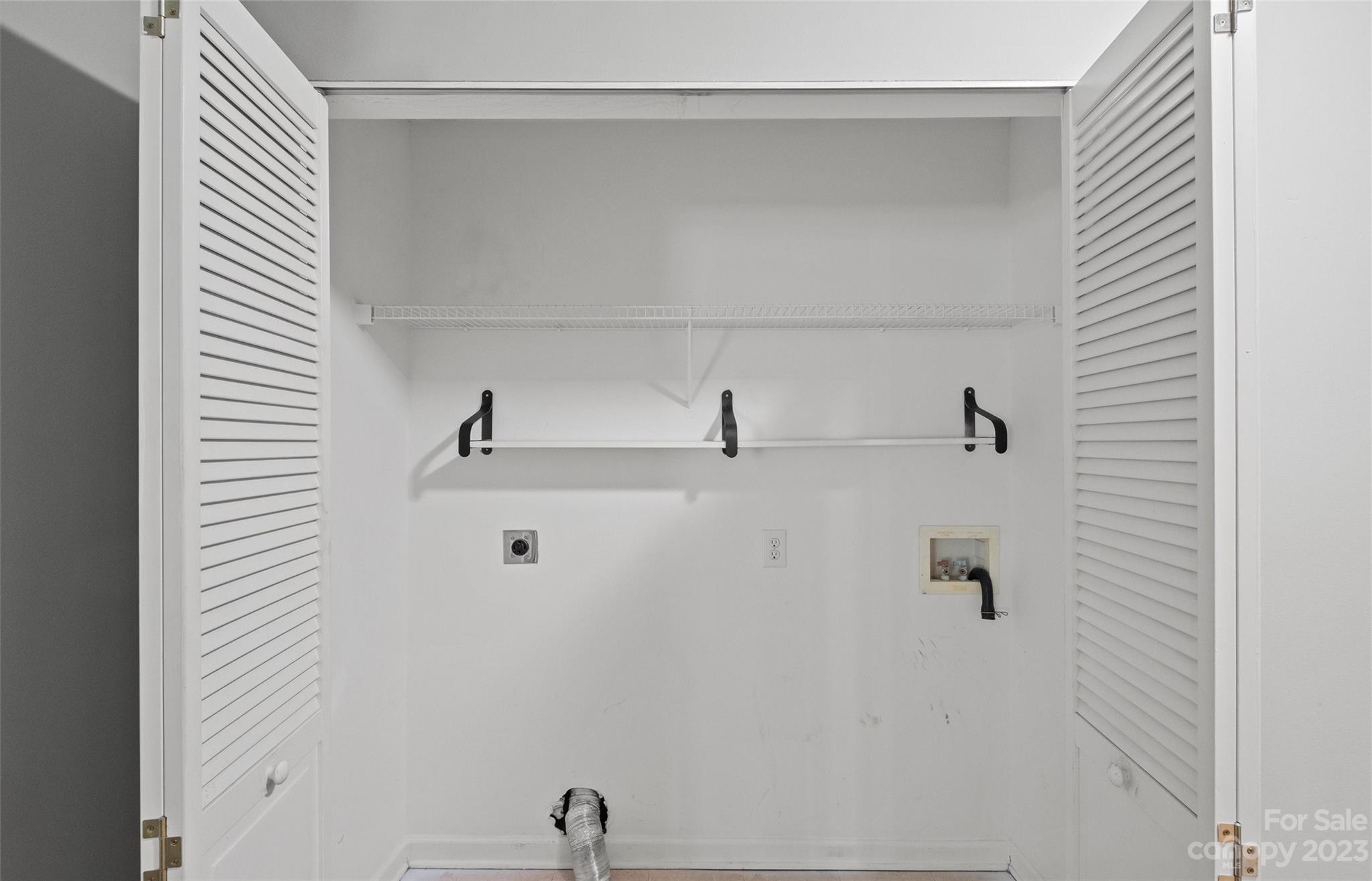 Empty laundry closet with open louvered doors, a wire shelf, hanging rod, and washer and dryer hookups.