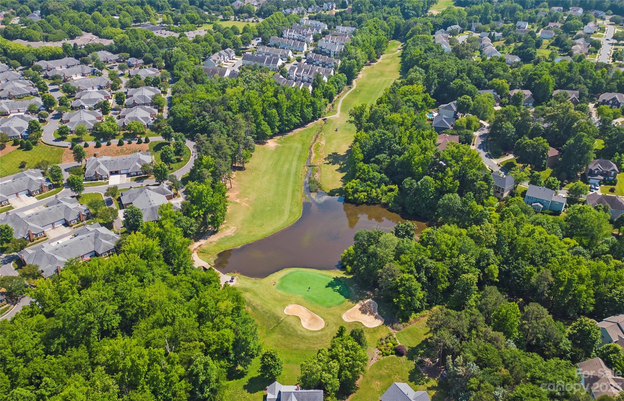 Aerial view of a golf course community with a pond, sand bunkers, and homes among mature trees.