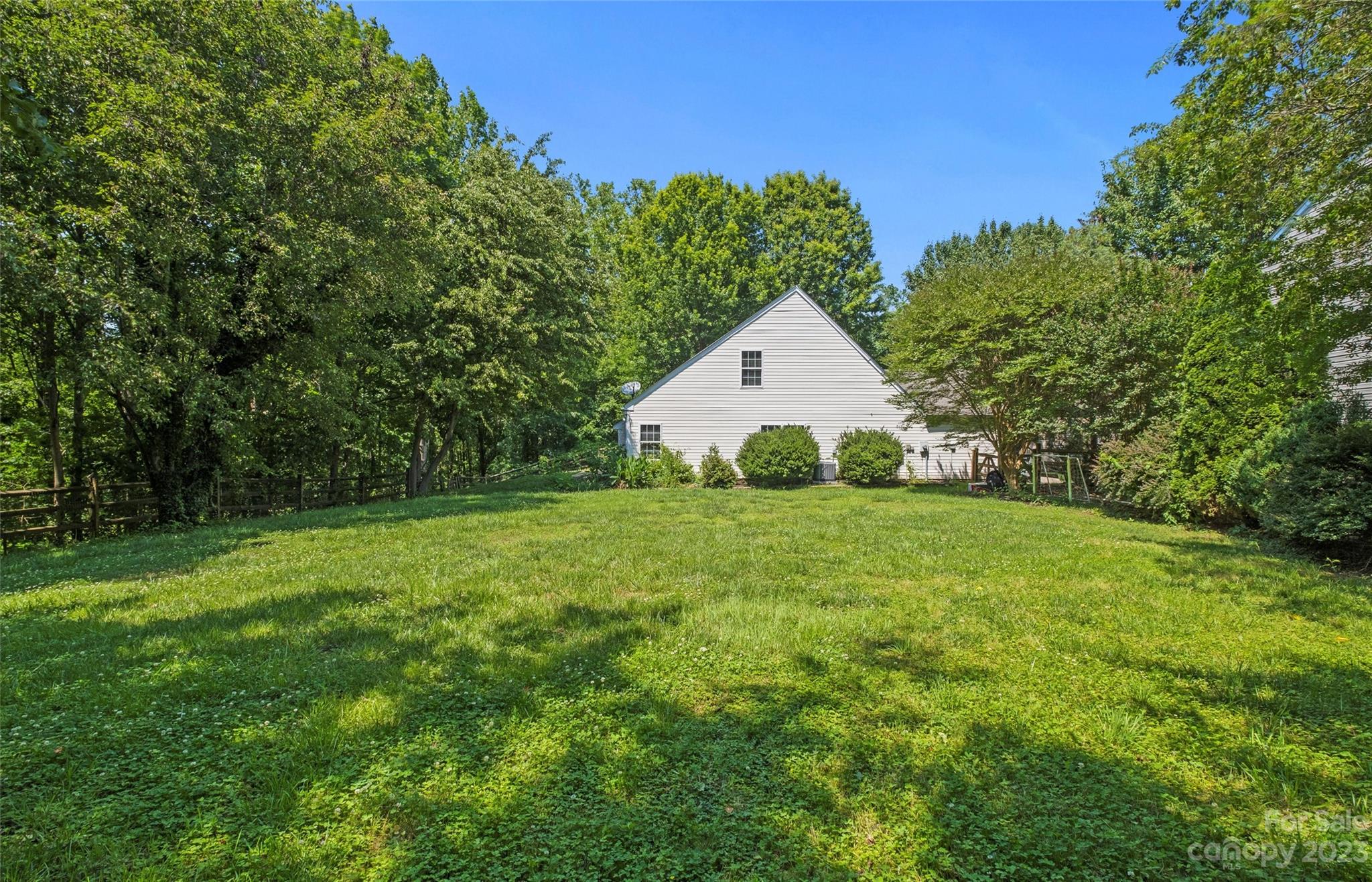 Grassy backyard and mature trees behind a white-sided house, with a wooden fence and swing set.