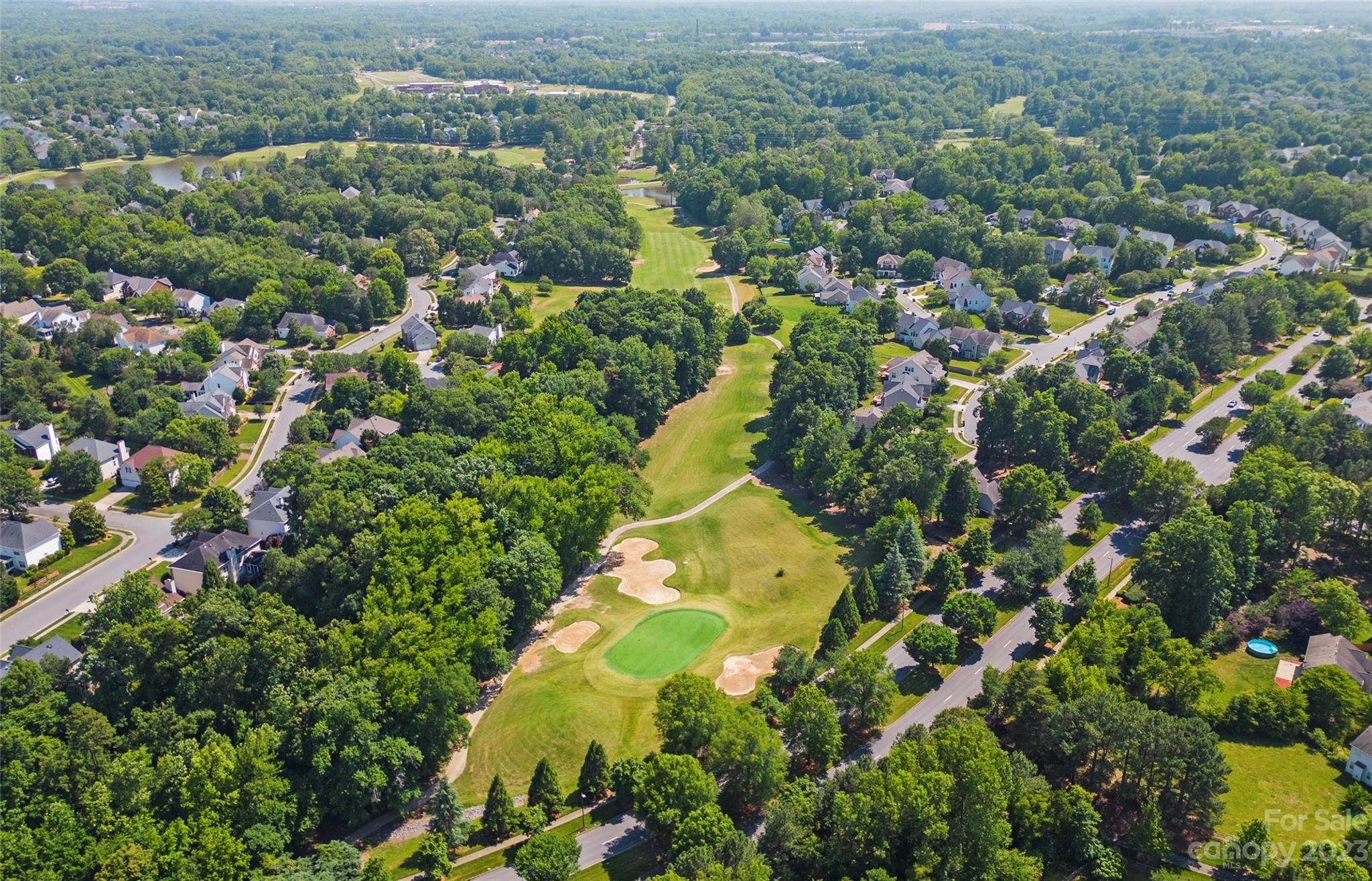 Aerial view of a tree-lined neighborhood beside a golf course with a putting green and sand bunkers.