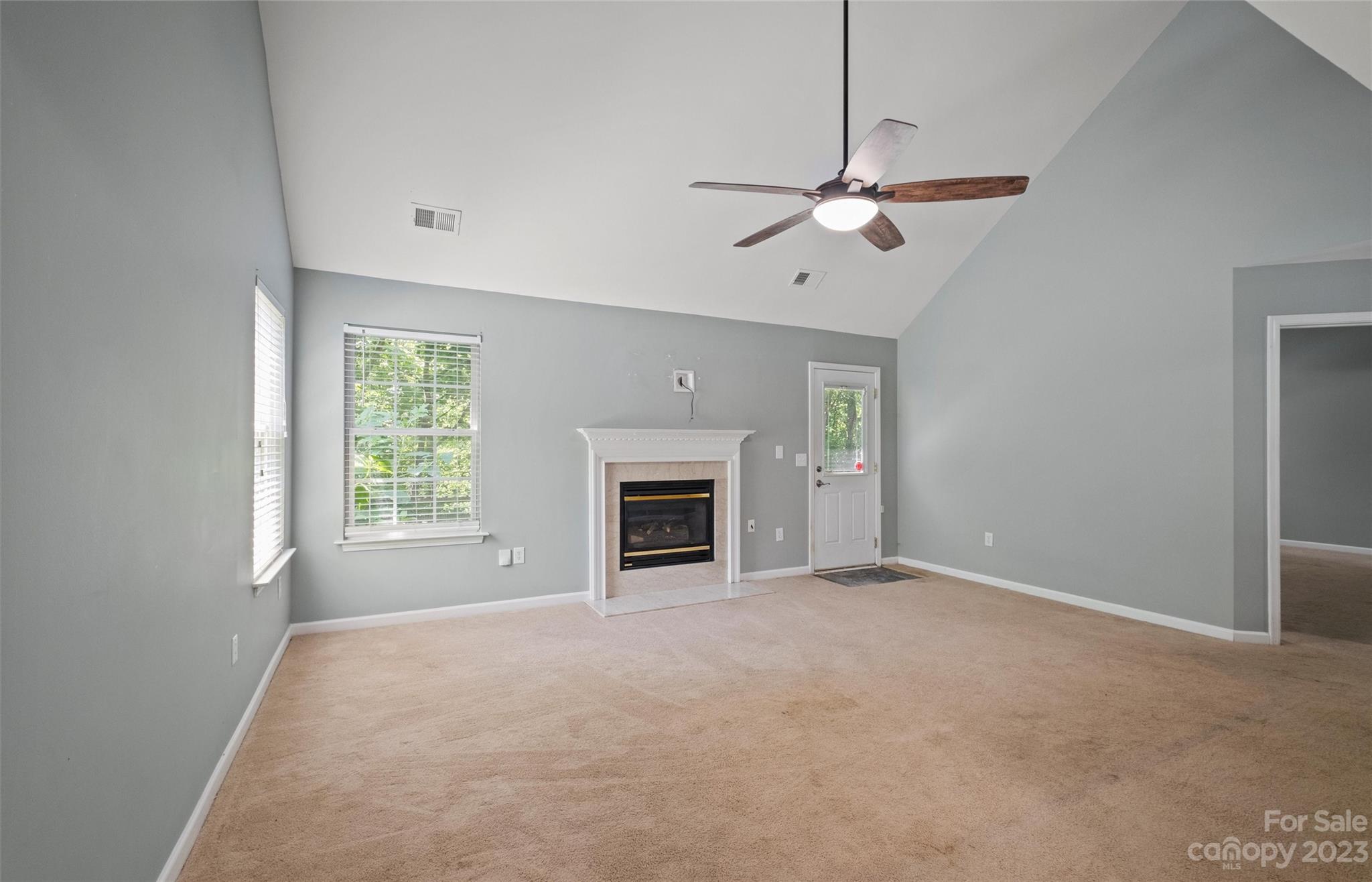Empty living room with a vaulted ceiling, ceiling fan, and white-mantel fireplace.